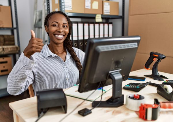 African woman working at small business ecommerce approving doing positive gesture with hand, thumbs up smiling and happy for success. winner gesture.